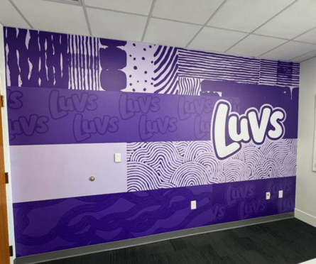 Office wall mural with bold purple patterns and large logo repeated across the design