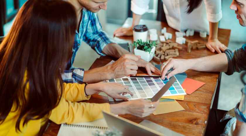 A group of colleagues collaborating on wall mural planning for their office space, selecting colors from swatches